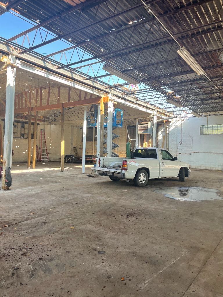 A white truck is parked under a roof in an empty building.