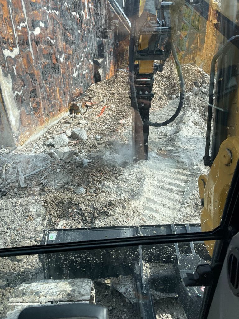 A bulldozer is breaking a concrete wall with a hammer.