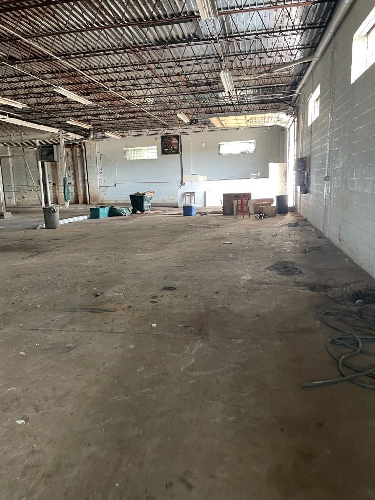 A large empty warehouse with a ceiling fan and boxes on the floor.