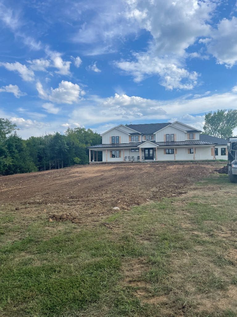 A large white house is sitting on top of a dirt field.