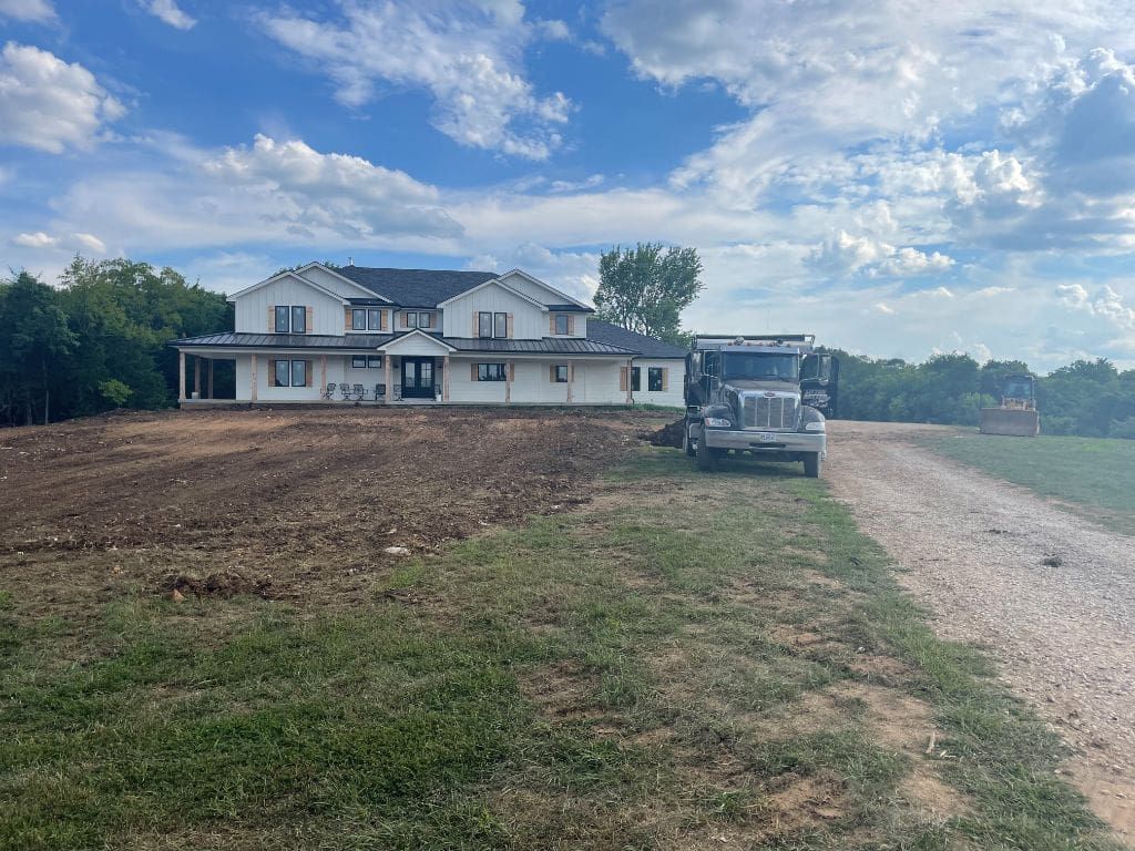 A truck is parked in front of a house on a dirt road.