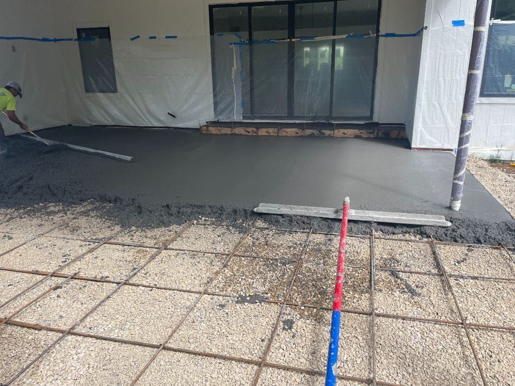 A man is laying concrete on a patio in front of a building.