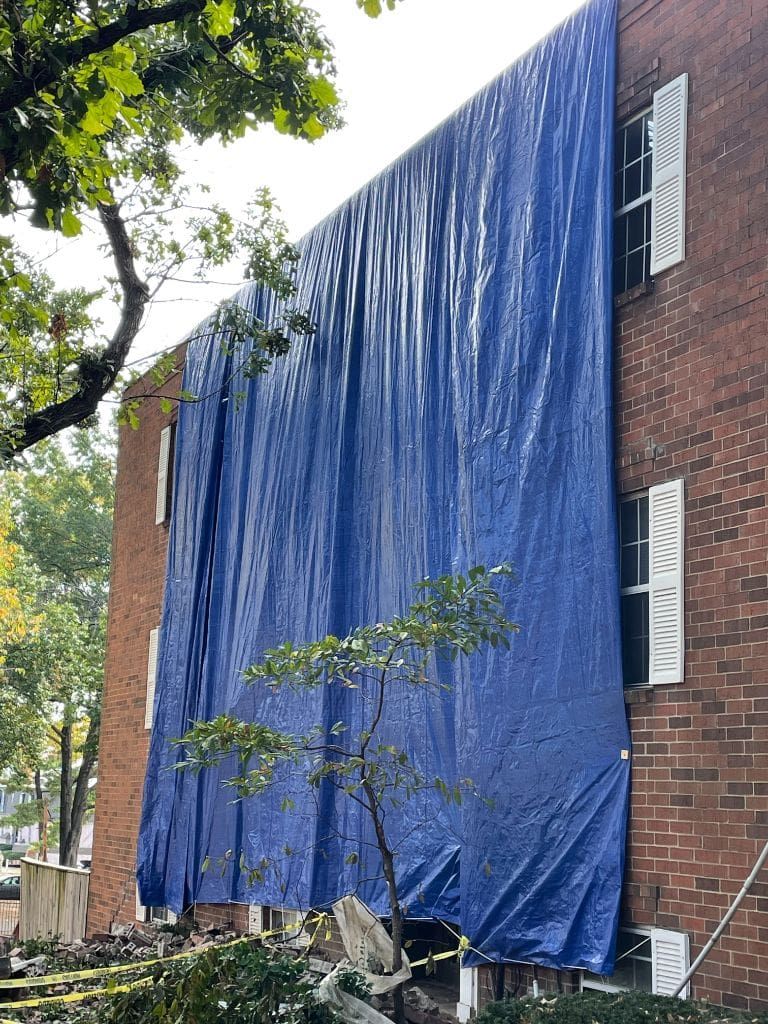 A large blue tarp is covering the side of a brick building.