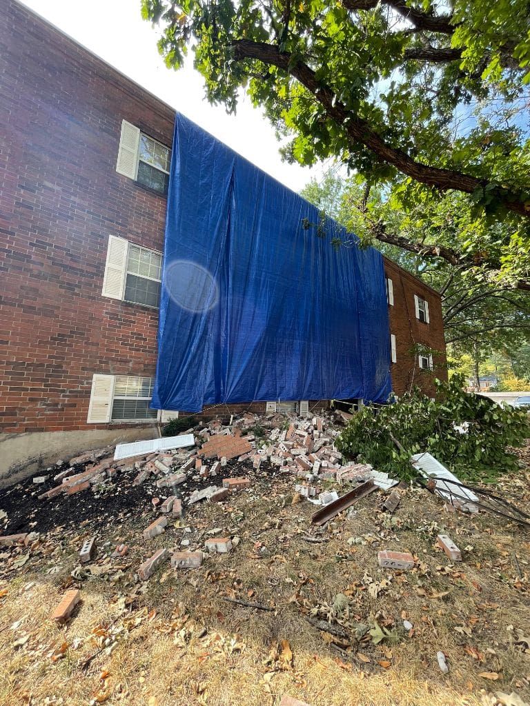 A brick building with a blue tarp covering it is being demolished.