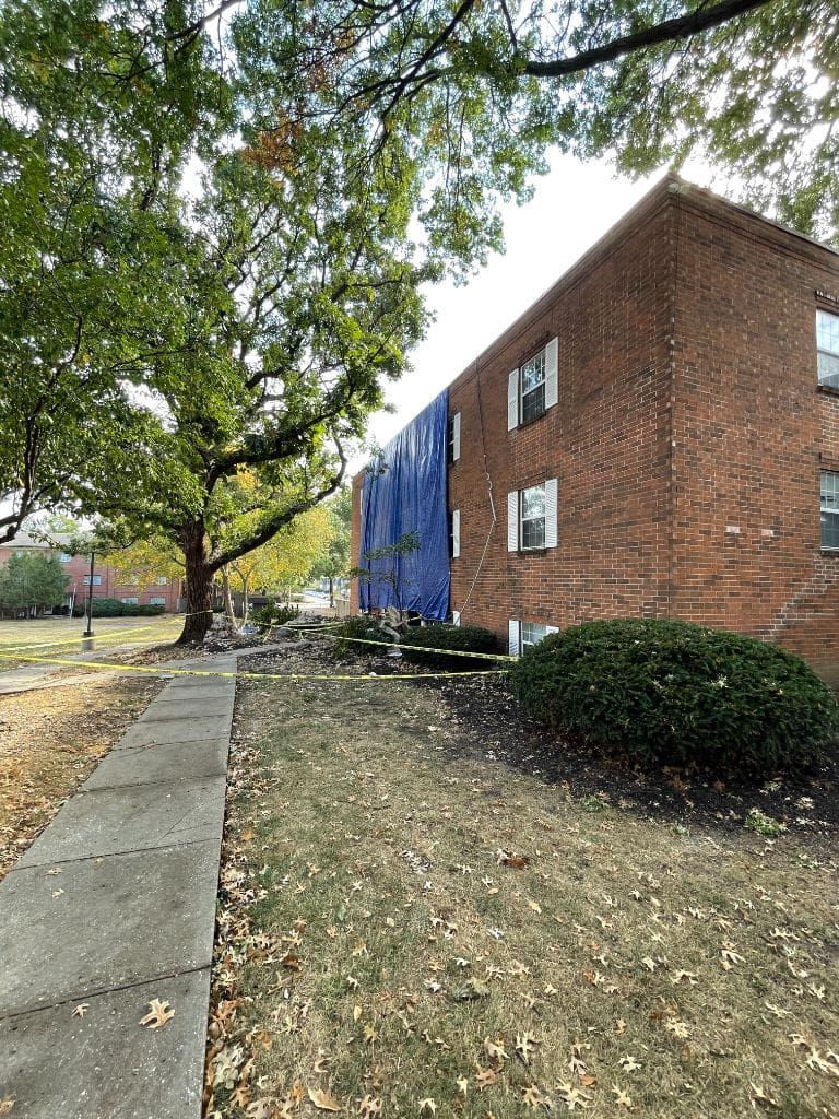 A brick building with a blue roof and a tree in front of it.
