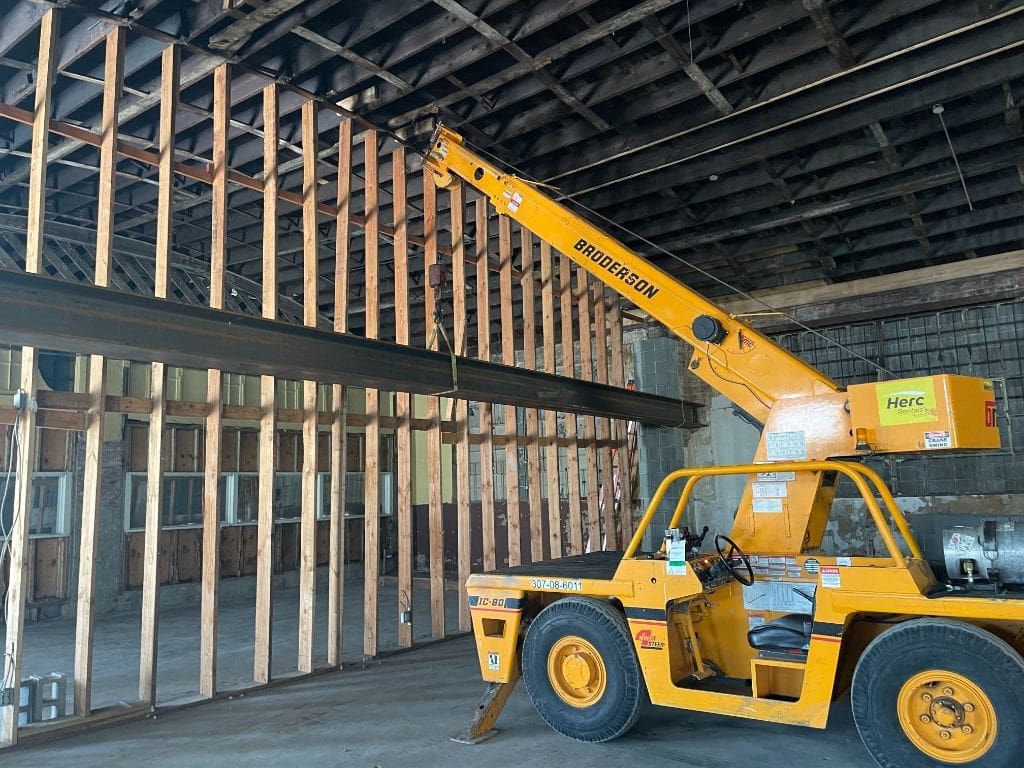 A yellow truck with a crane attached to it is in a building under construction.