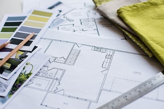 A collection of house plans, color swatches, pencils, and fabric swatches arranged on a flat surface, used for interior design.