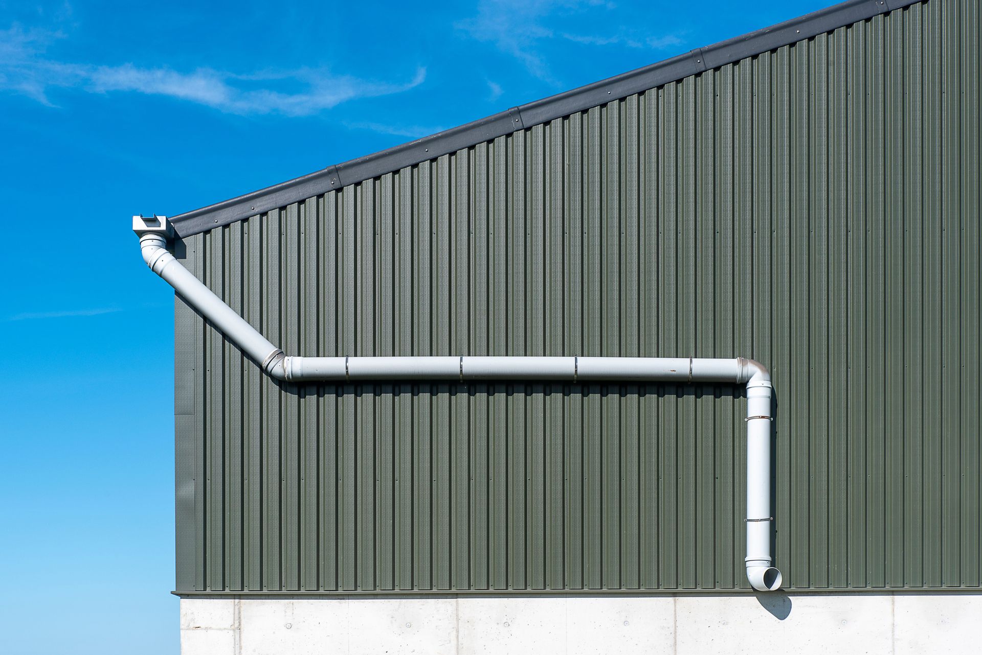White downspout and gutter on a green metal building against a blue sky