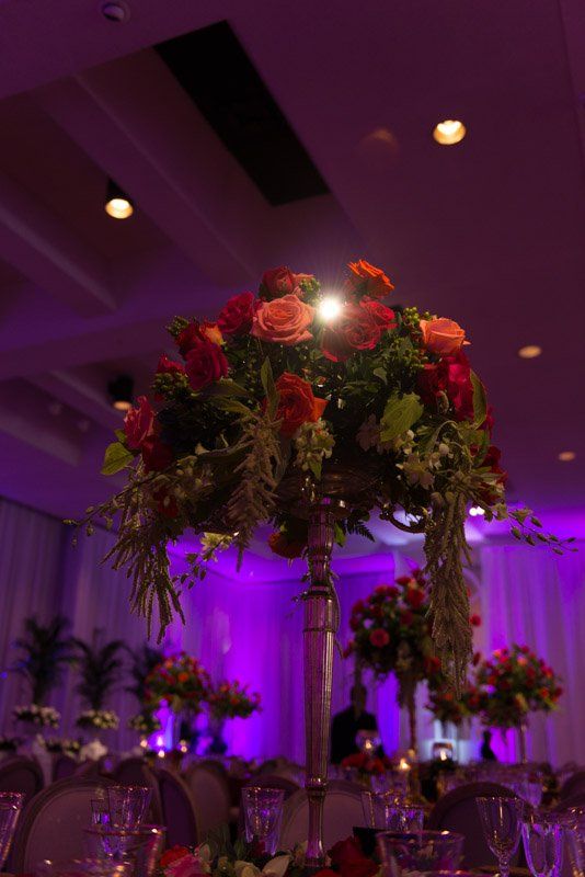 Elegant floral centerpieces on a table in a dimly lit room, with purple lighting.