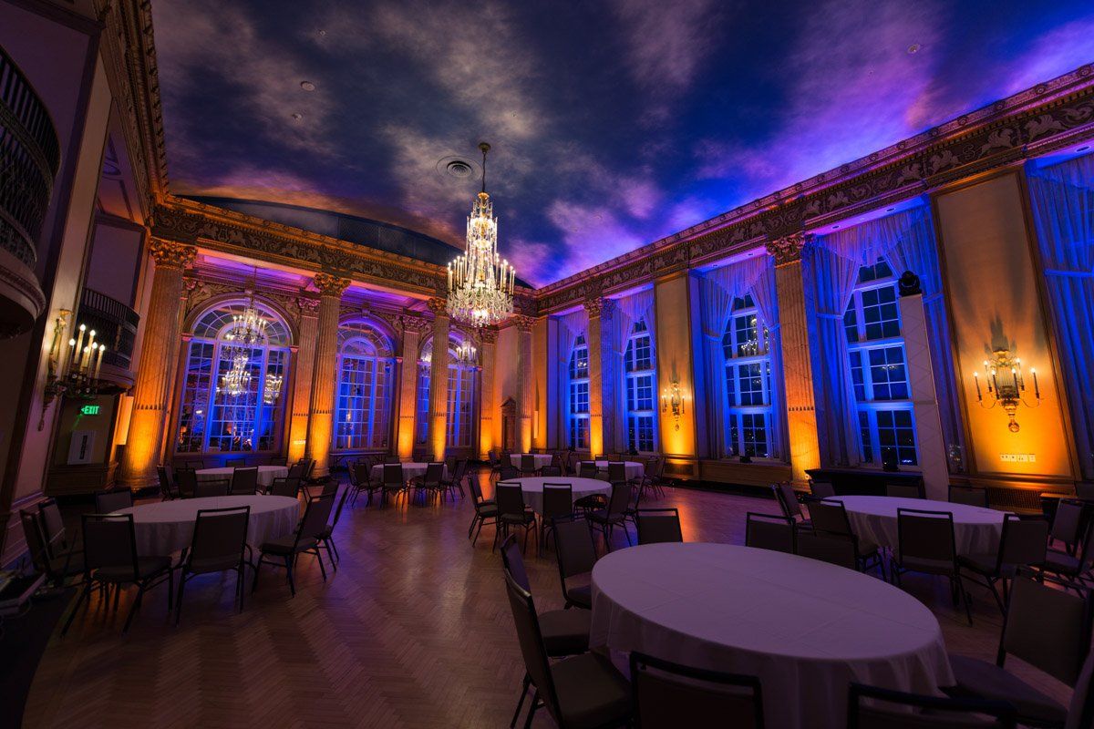 Elegant ballroom with round tables, chairs, and dramatic lighting in blue and orange.
