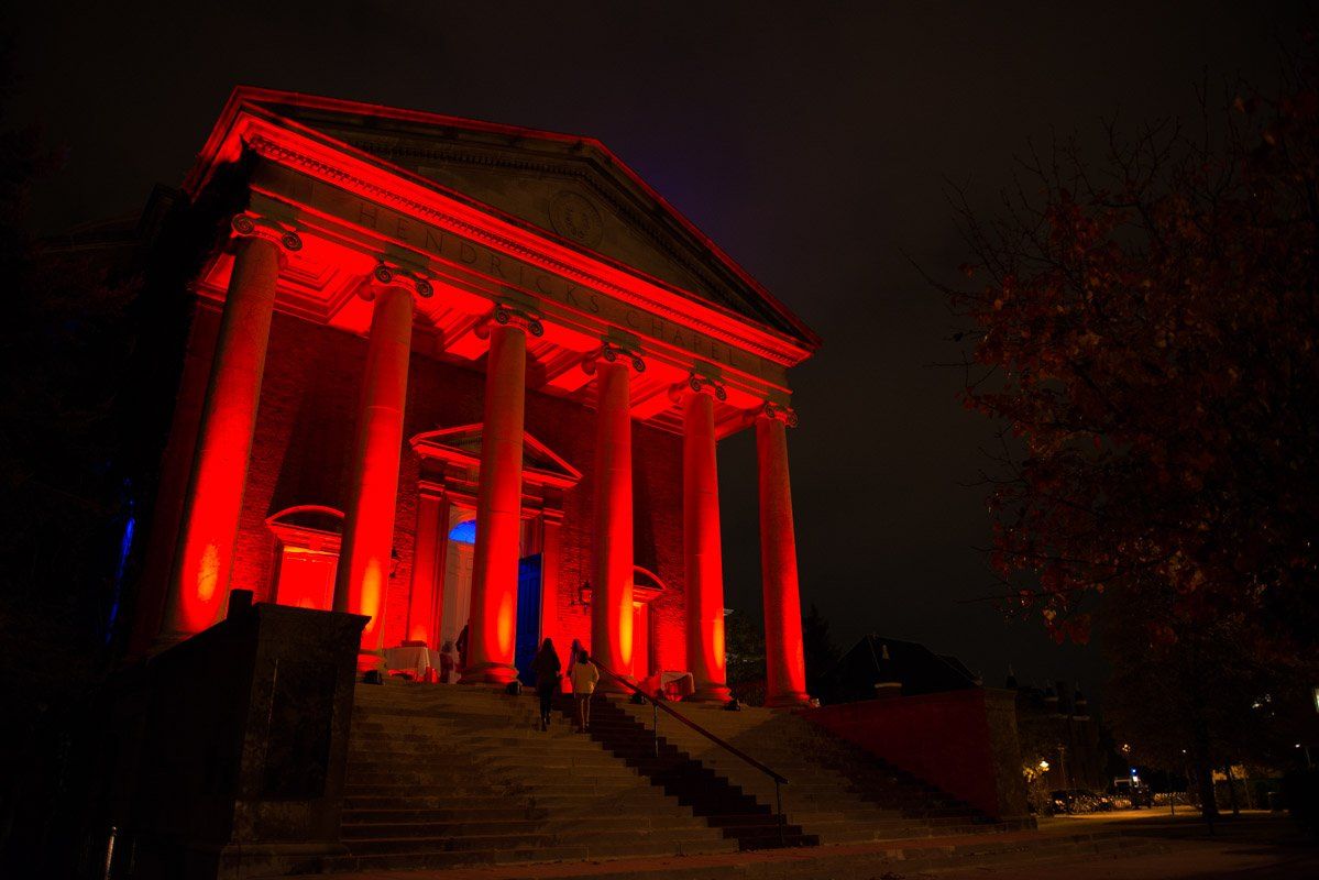 A building with large columns is illuminated in red light at night.