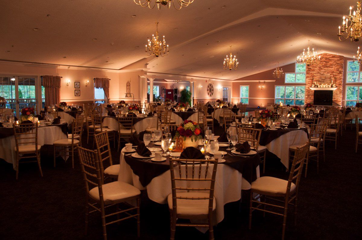 Elegant banquet hall with round tables set for a formal event; gold chairs, dark tablecloths, and warm lighting.
