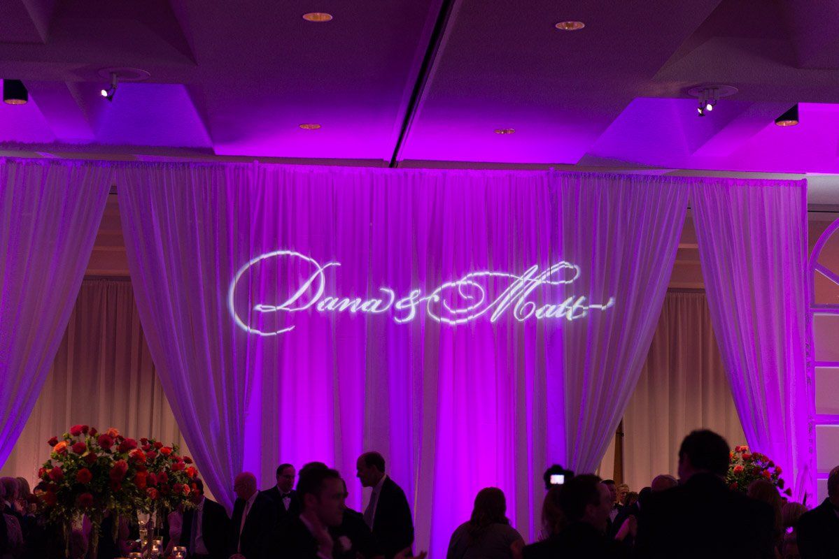 Purple-lit wedding reception backdrop with white draping and names 