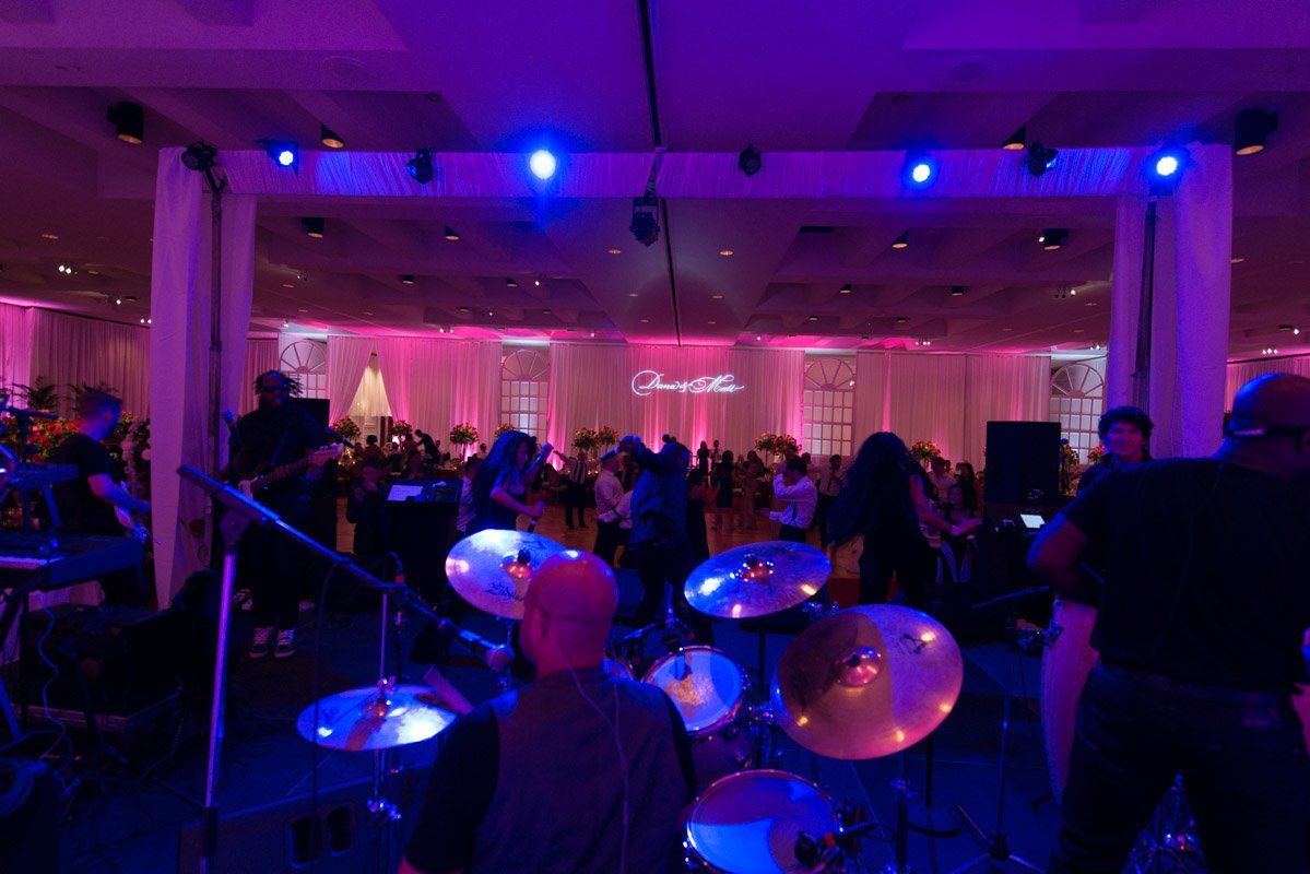 Band performing on stage at an event. Pink and blue lighting, audience in background.