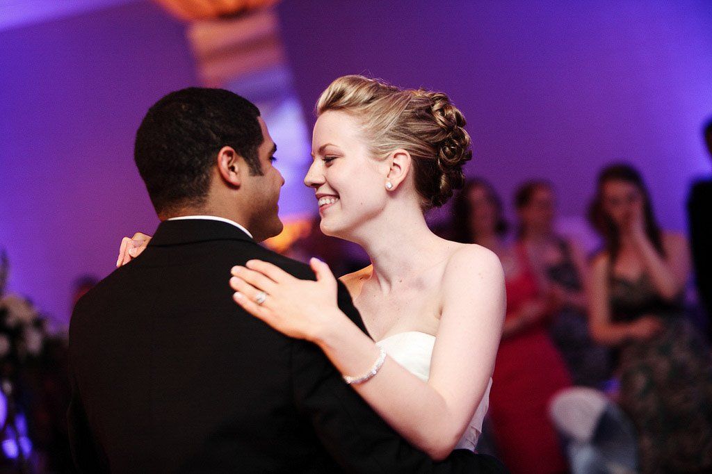 Bride and groom dancing at their wedding, smiling, with purple uplighting.