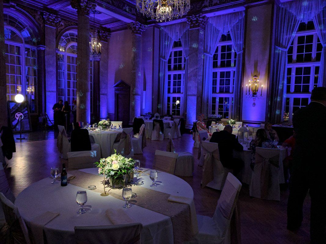 Formal ballroom with round tables set for an event, illuminated by blue uplighting.