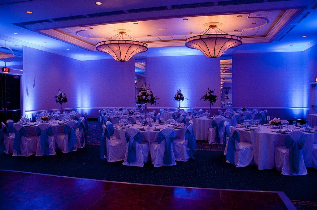 Wedding reception with tables and chairs in a room lit with blue and orange lights.