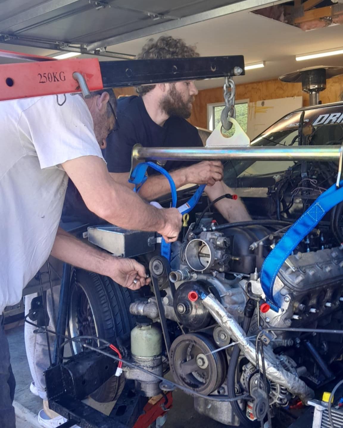 Two men are working on a car engine in a garage