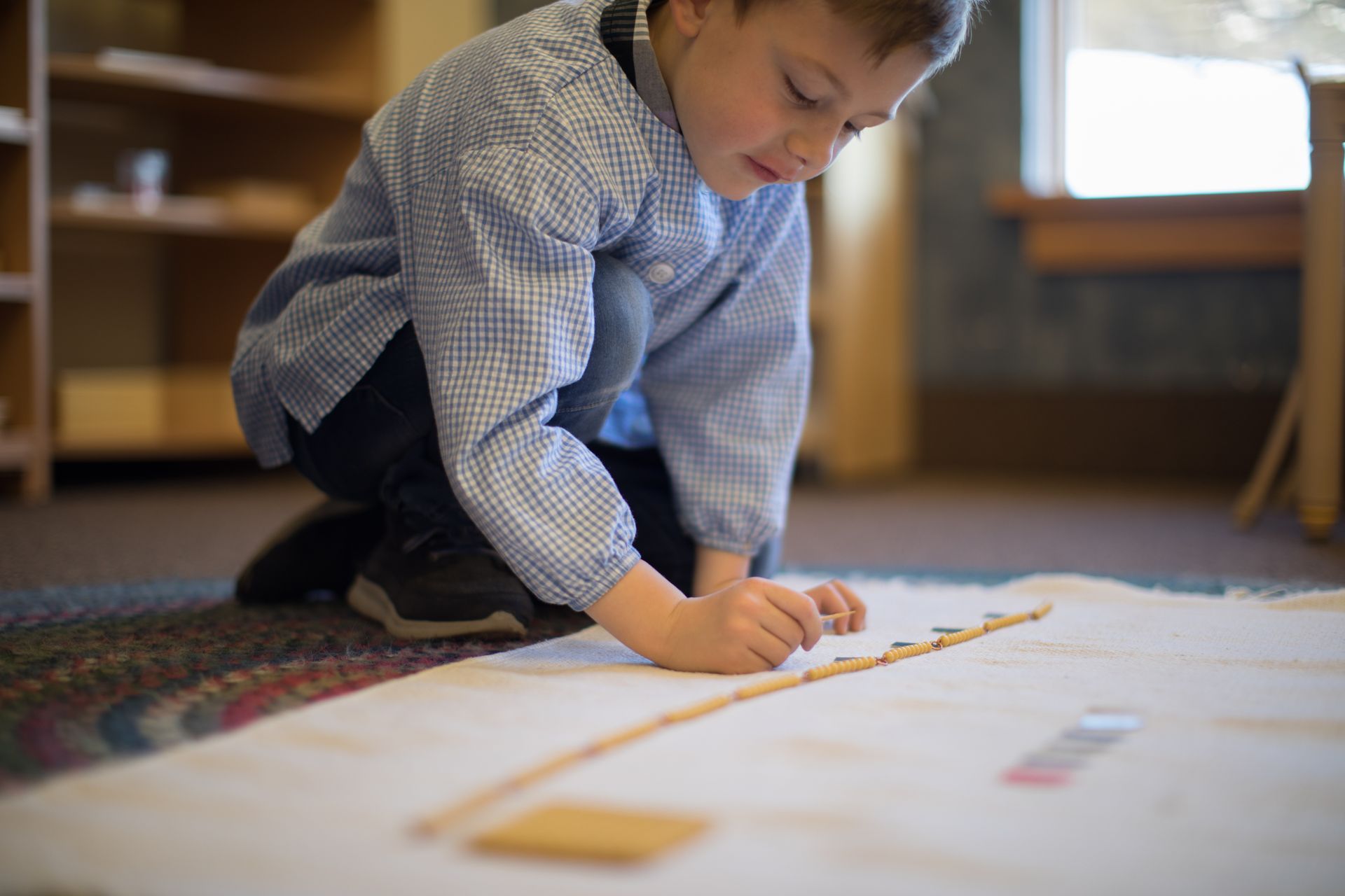 Child kneeling on a carpet, carefully arranging blocks on a long white paper strip indoors