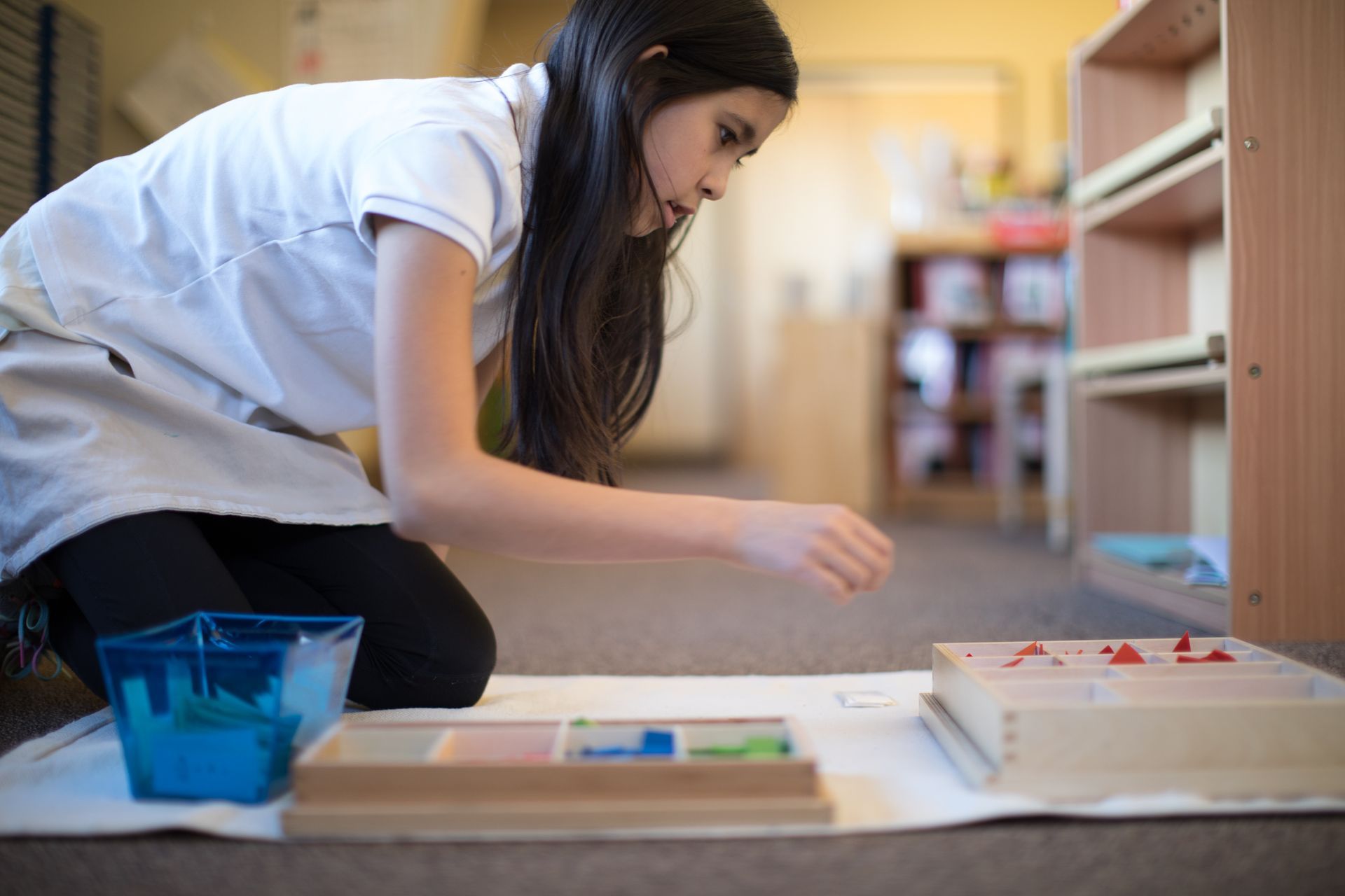 Person kneeling on the floor painting at a low table with trays and supplies in a room