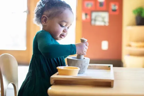 A little girl is playing with a mortar and pestle at a table.