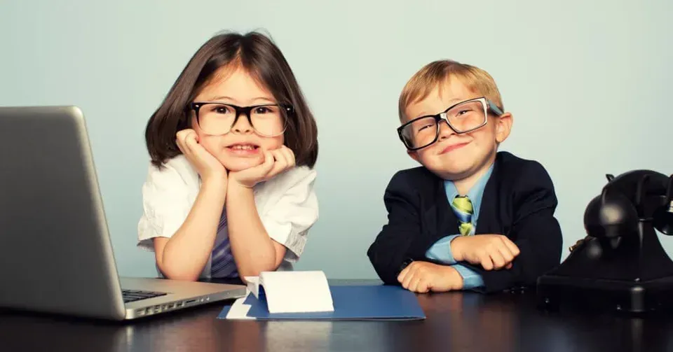 A boy and a girl are sitting at a desk with a laptop.