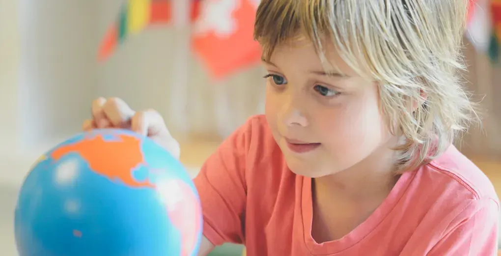 A young boy is looking at a globe in a classroom.