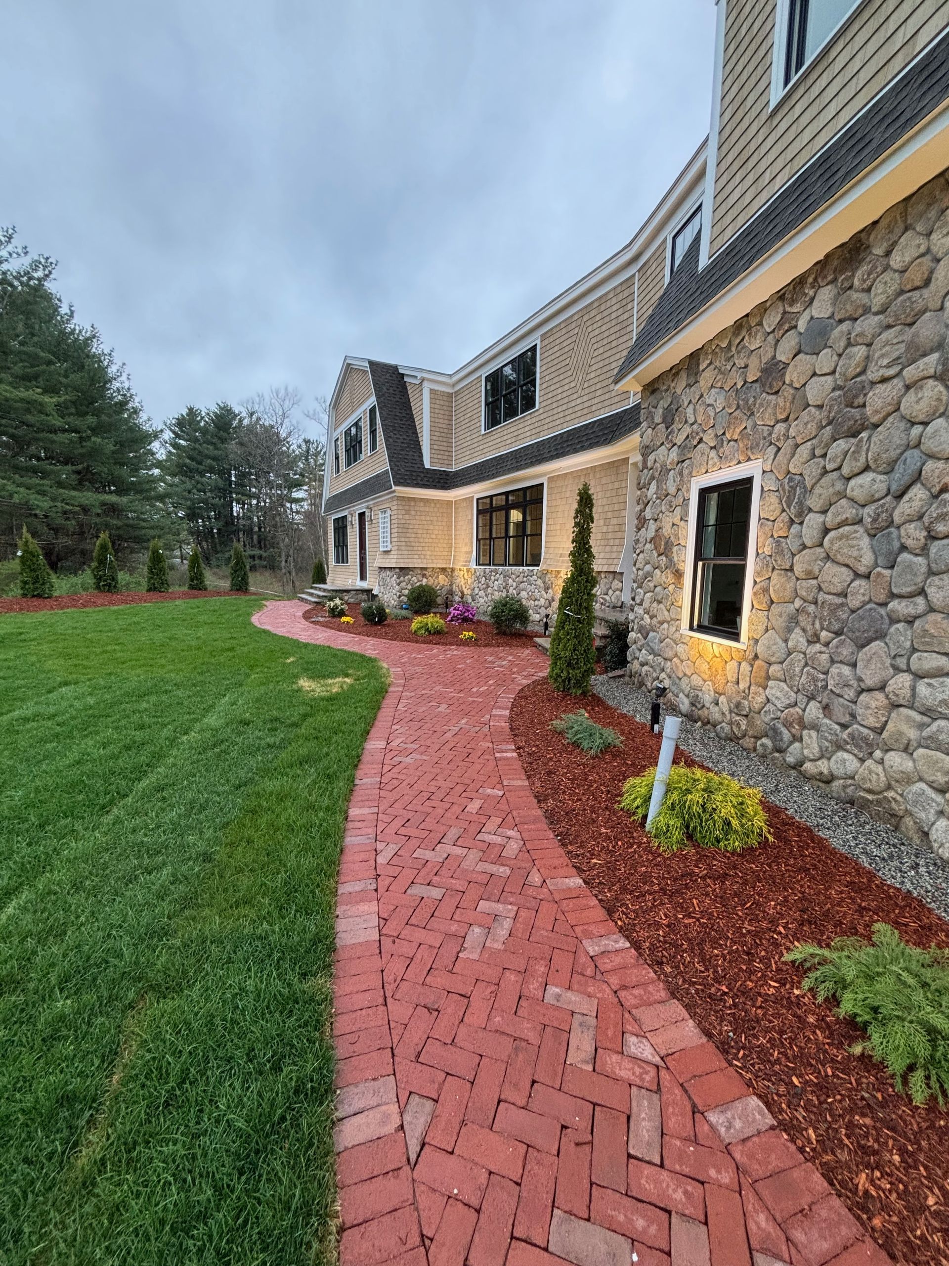 A red brick walkway leading to a large stone house.