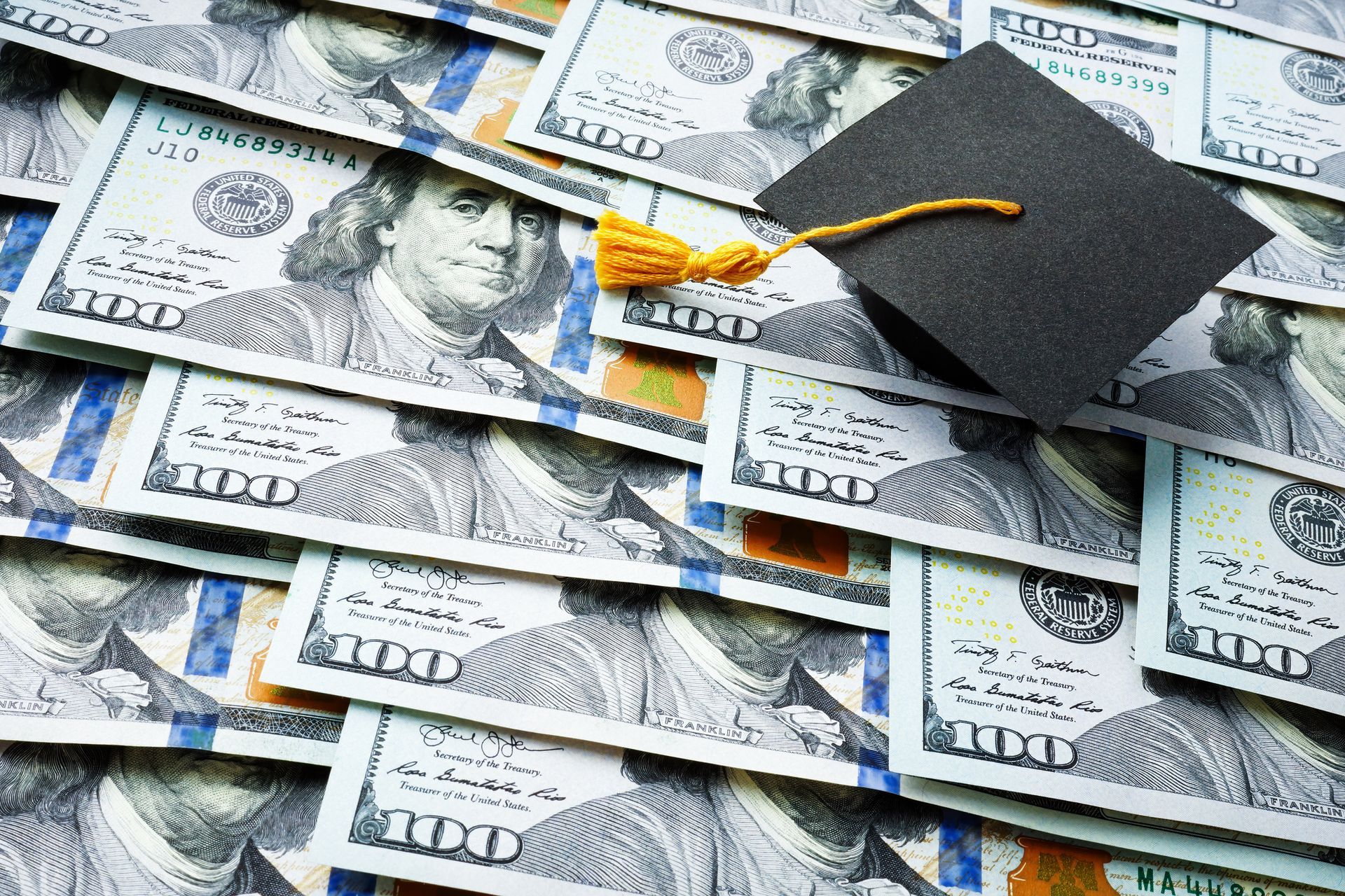 A graduation cap is sitting on top of a pile of money.