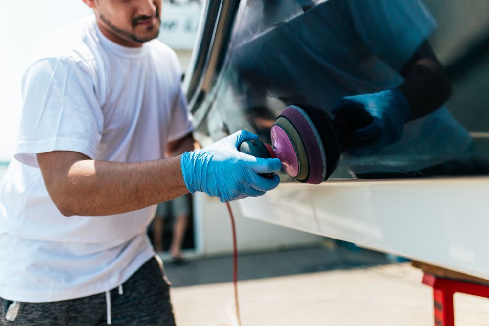 Man polishing a white boat hull with an electric buffer