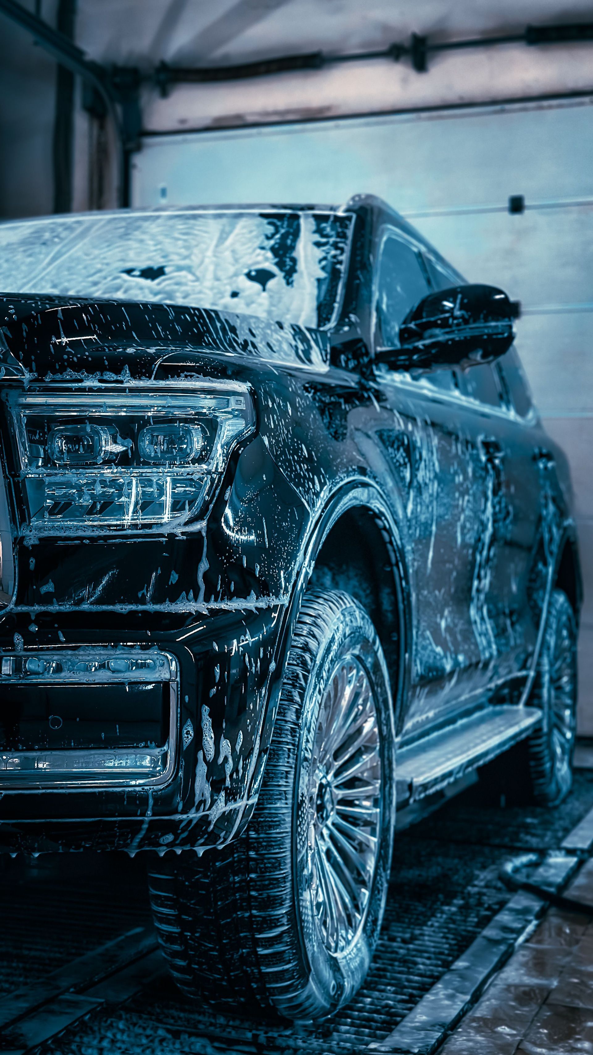 Black SUV being washed with soap in an indoor car wash bay