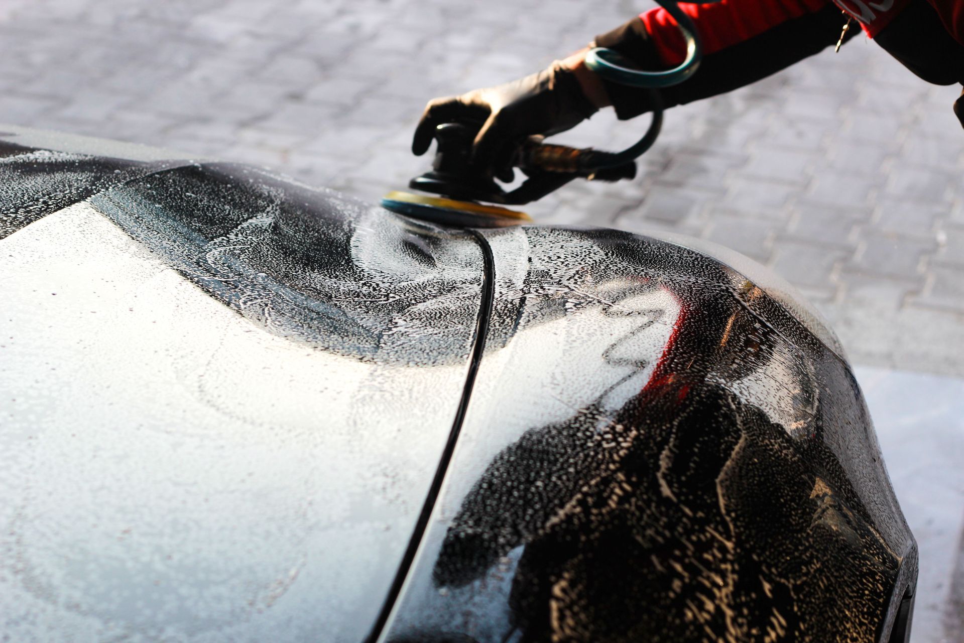 Gloved hand scraping ice from a car windshield with a yellow-edged tool