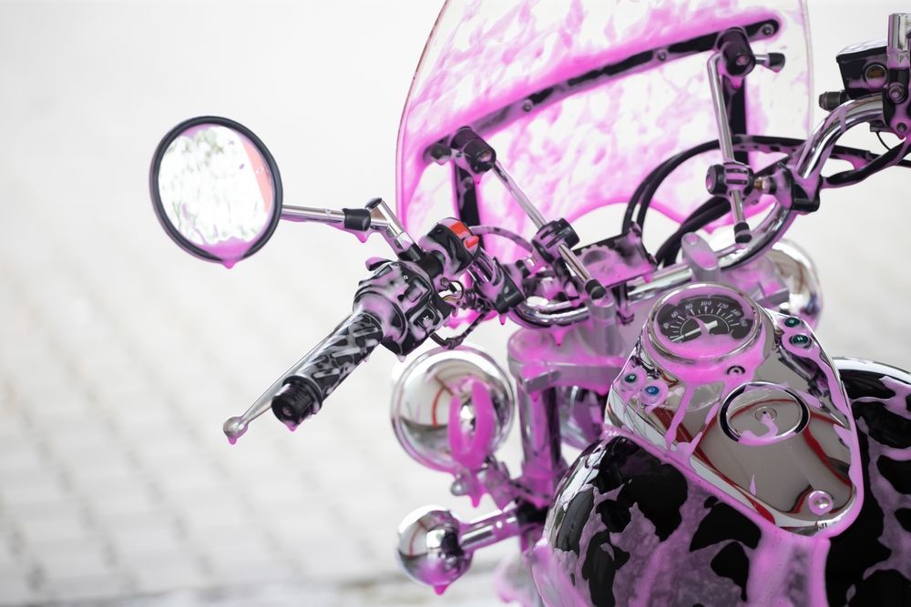 Pink and silver motorcycle handlebars and mirror against a white background