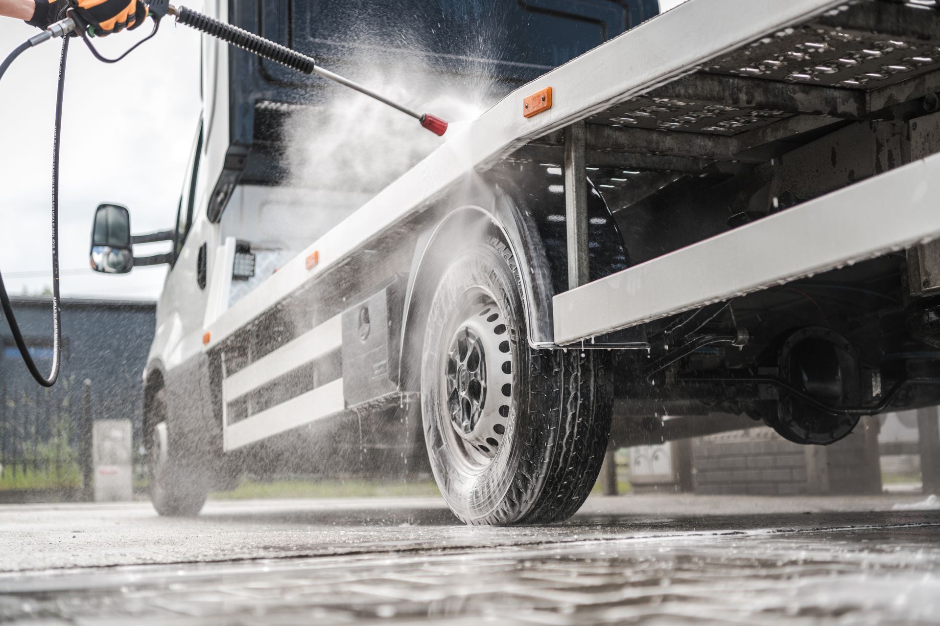 Pressure-washing the side and wheel of a white truck outdoors