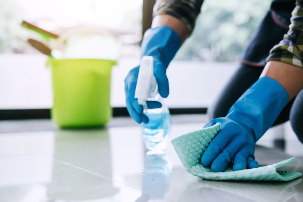 A Person Wearing Blue Gloves Is Cleaning The Floor With A Cloth And Spray Bottle — DP Cleaning Supplies Pty Ltd In Mareeba, QLD