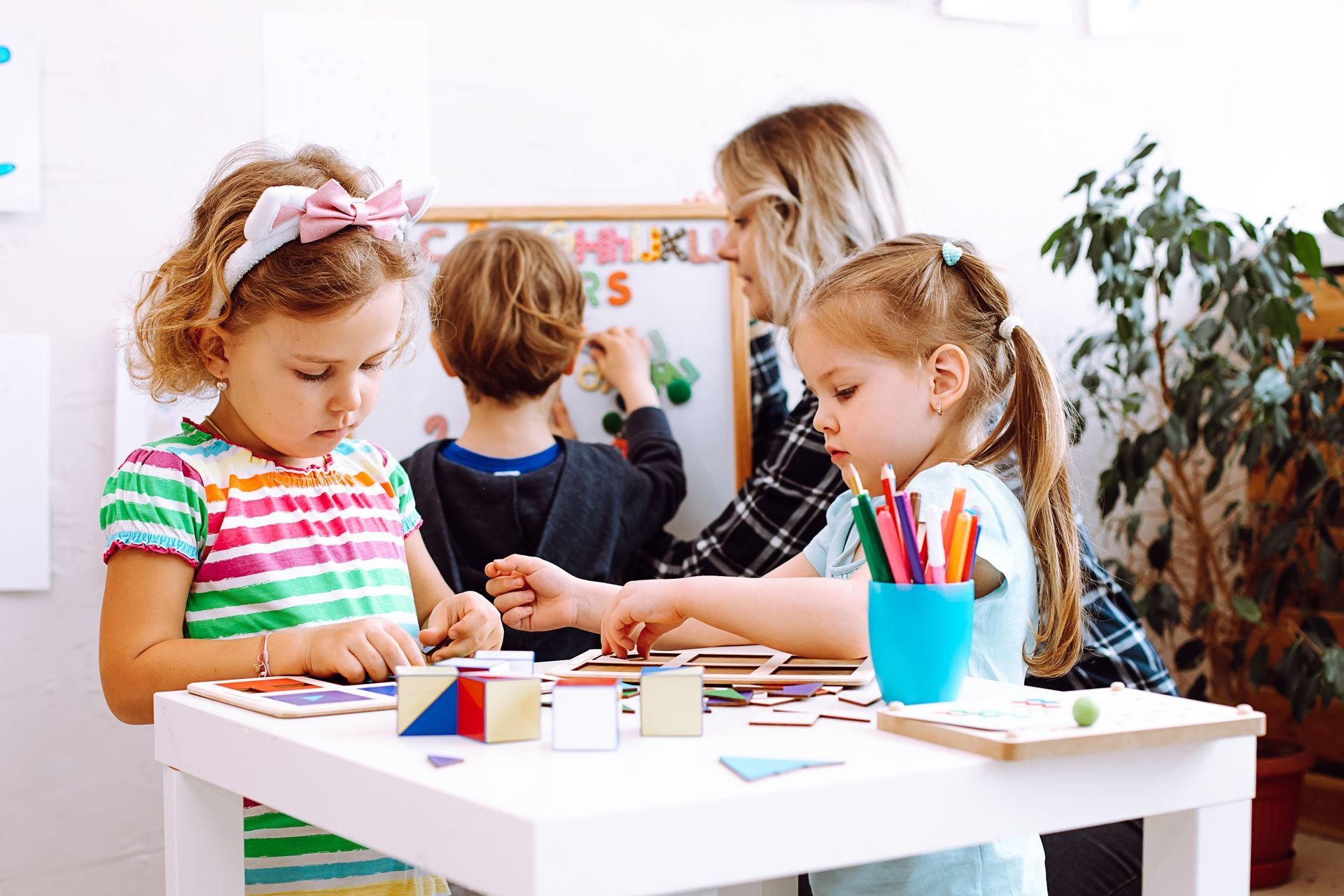 Young children exploring geometric shapes with an educator guiding them.