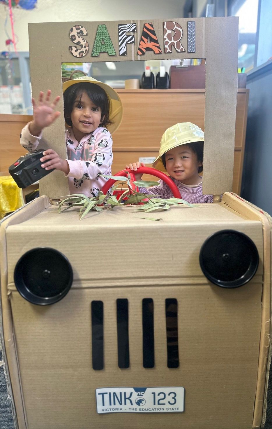 Two children in a cardboard safari jeep with a 