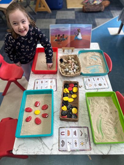 Girl smiling at sensory table with sand, rocks, and small trays.