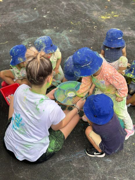 Children and adult play with colorful chalk on the ground. Everyone covered in chalk dust.