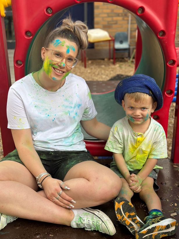 Woman and child covered in colorful paint at playground, smiling.