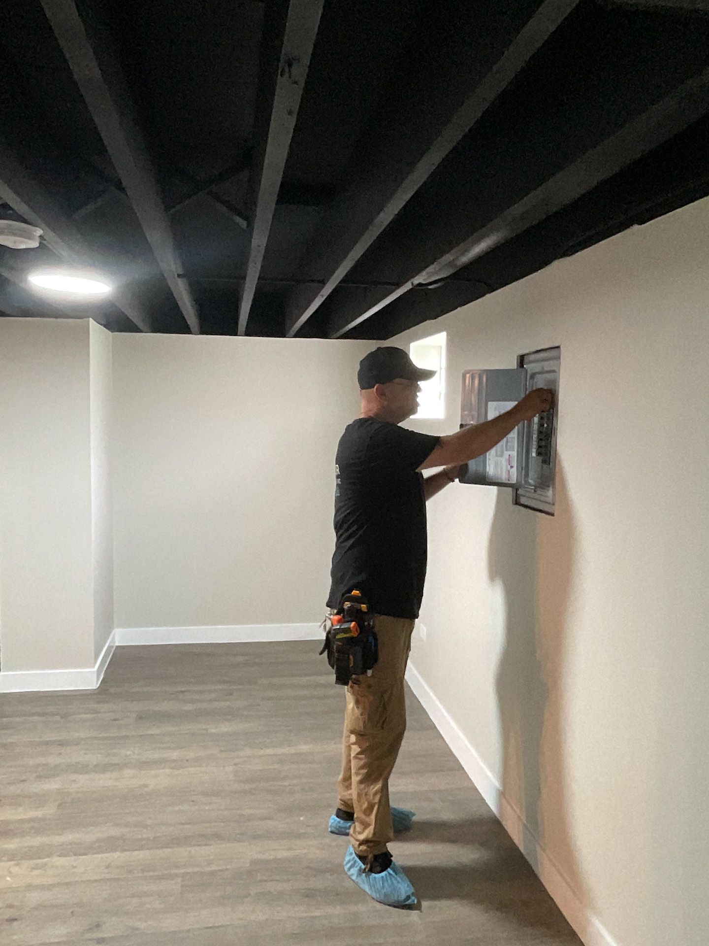 A man is working on an electrical box in a basement.