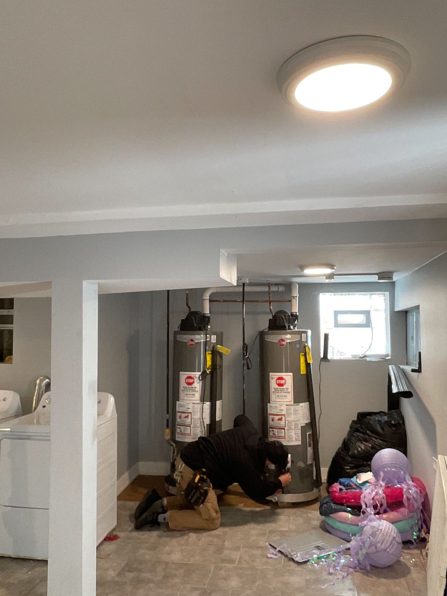 A man is working on a water heater in a basement.