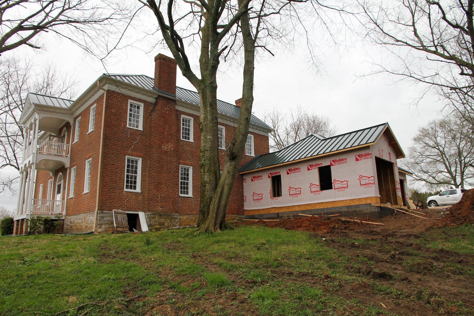 Red brick house beside a small shed under construction on a grassy, wooded slope