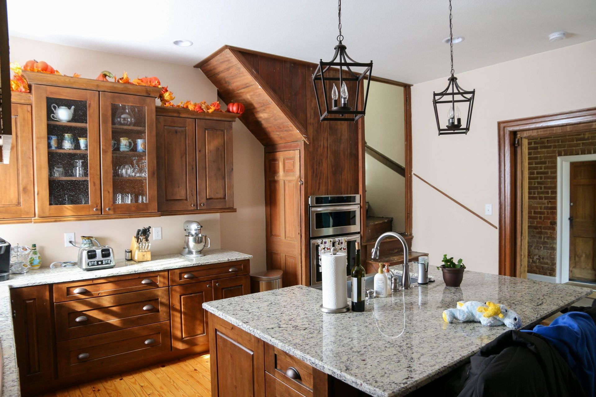 Modern kitchen with wooden cabinets, granite island, and autumn decor by a staircase