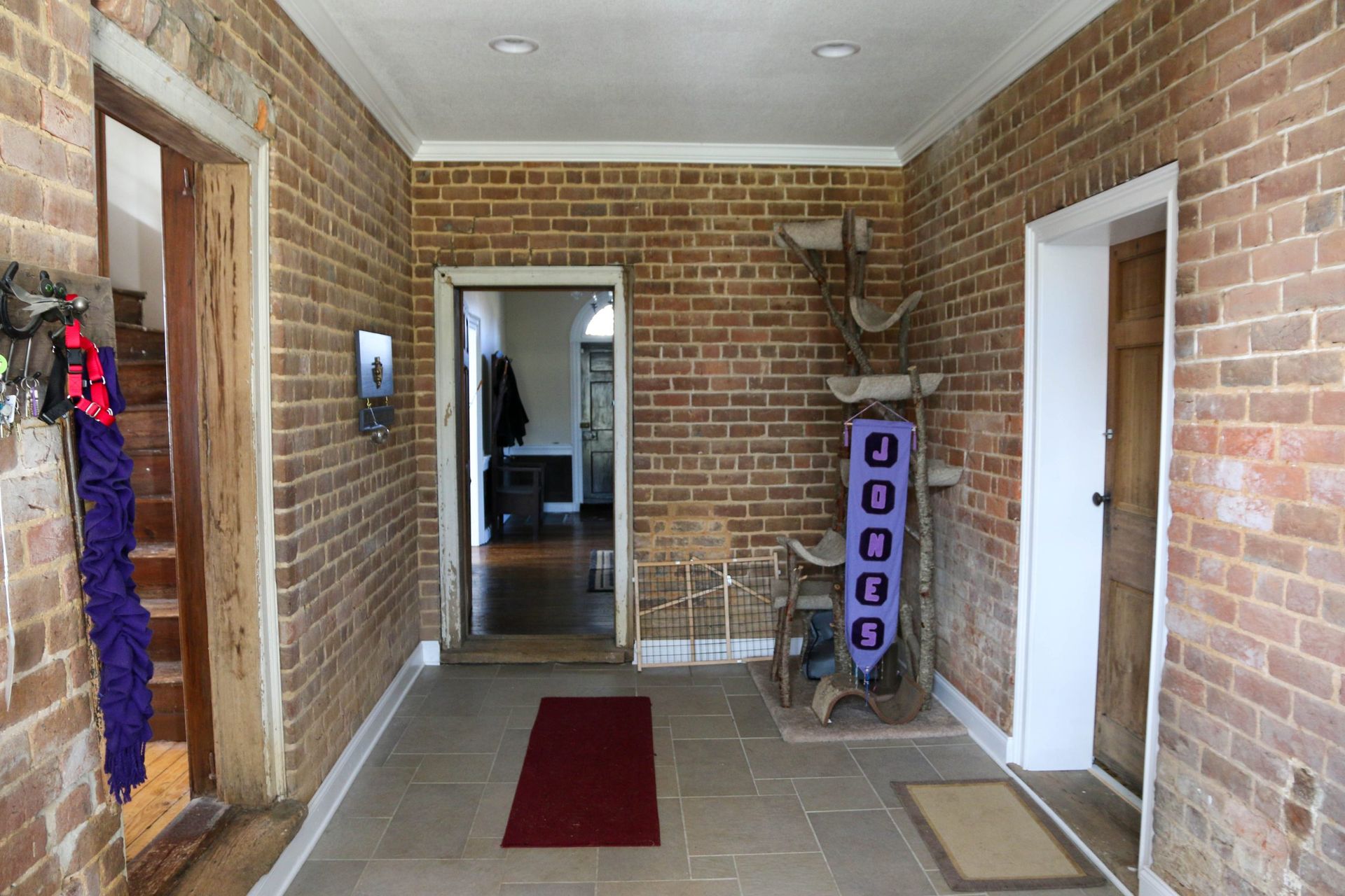 Covered brick porch with tiled floor, red runner, doorway to interior, and umbrella stand with purple umbrellas