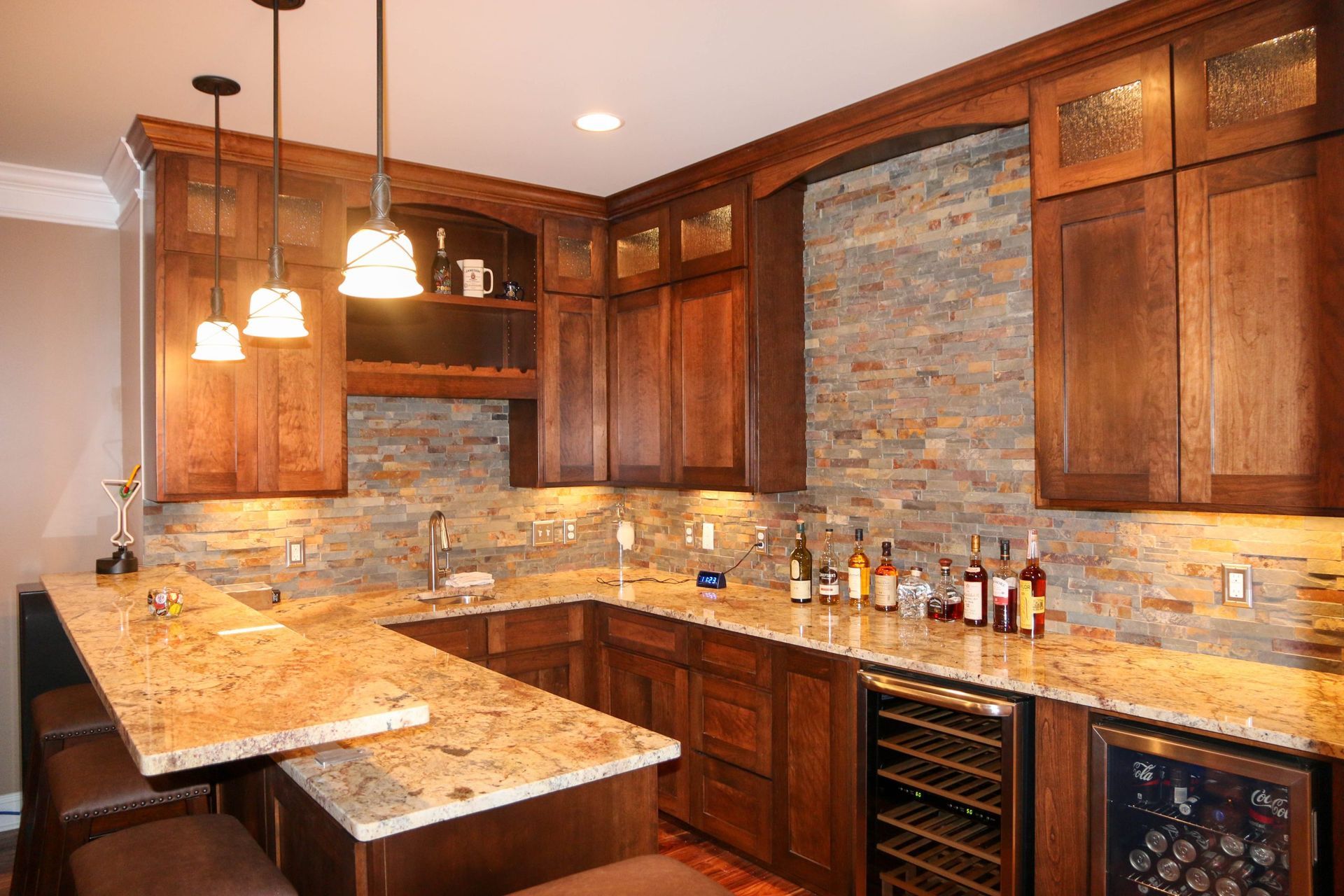 Warm-toned kitchen with dark wood cabinets, granite countertops, pendant lights, and a stone backsplash.