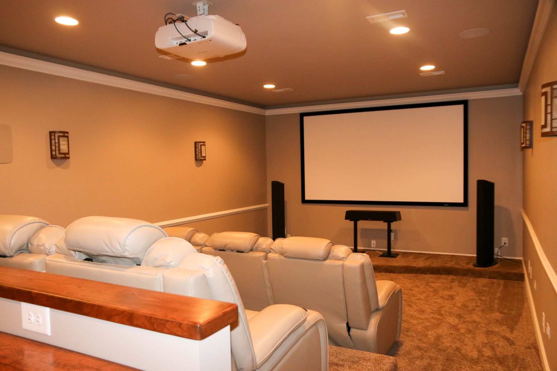 Home theater room with beige recliners, projector screen, wall speakers, and recessed lighting