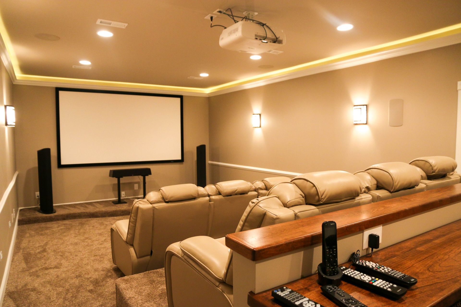 Home theater room with beige recliners, large projector screen, wall sconces, and a snack table