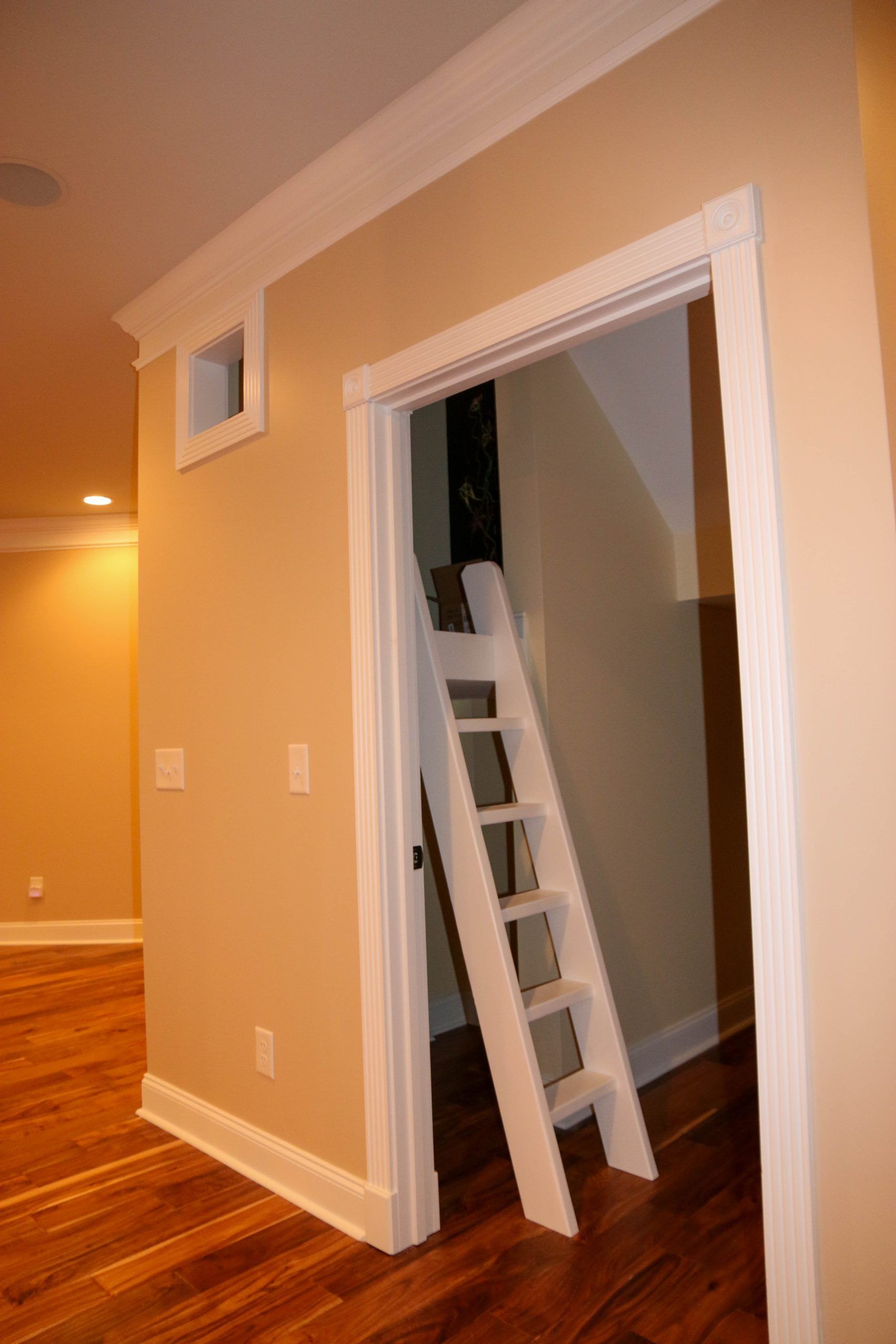 Hallway with hardwood floor and a white ladder leading into a small open attic doorway