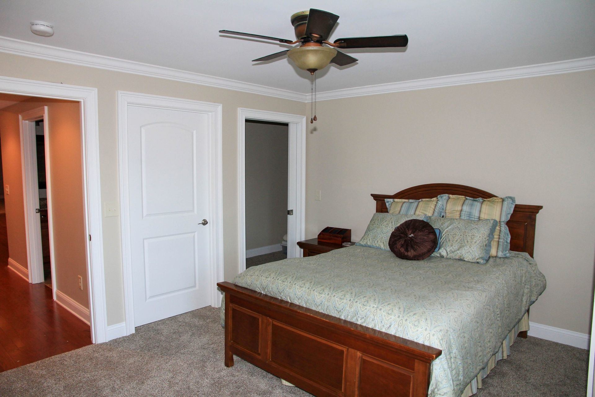 Bedroom with a wooden bed, beige walls, white doors, and a ceiling fan.